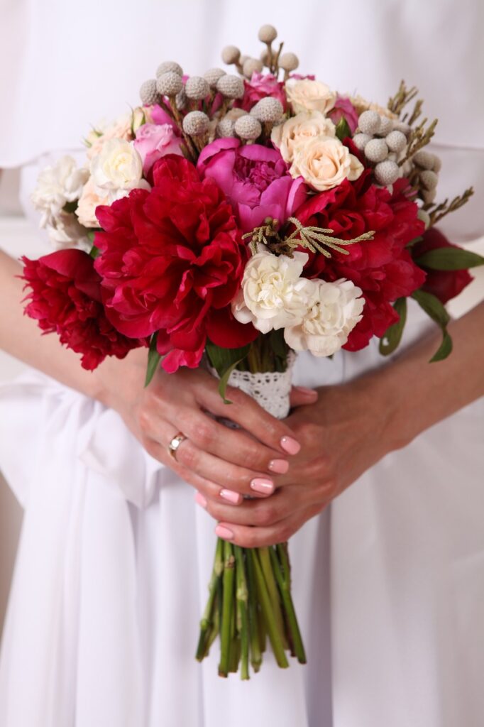 A girl in a wedding dress holding a pink and red wedding bouquet.
